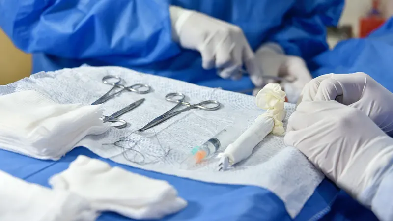 Mains gantées et instruments chirurgicaux posés sur un champ opératoire.