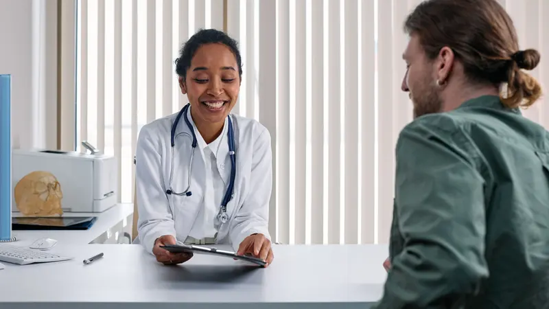 Une médecin en consultation échange avec un patient assis face à son bureau.